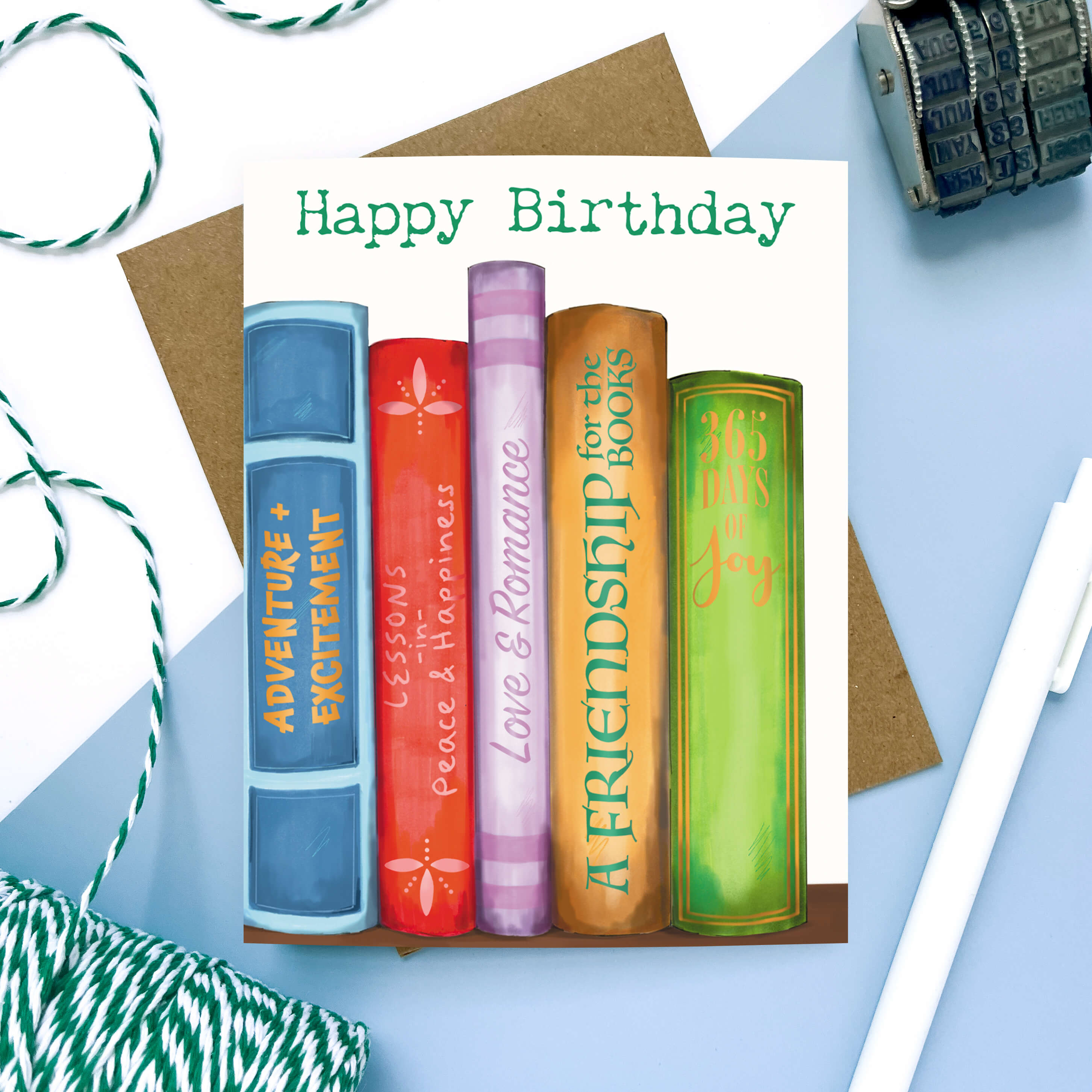 Birthday card featuring colorful illustrated book spines with fun messages like "Adventure + Excitement" and "Love & Romance."
