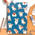 Notebook with marker illustrations of corgis on a teal background.