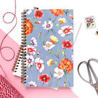 Illustrated floral notebook with cosmos flowers on a blue background.