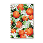Notebook with orange fruit and white orange blossoms on a green background.