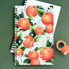 Notebook with orange fruit and white orange blossoms on a green background.
