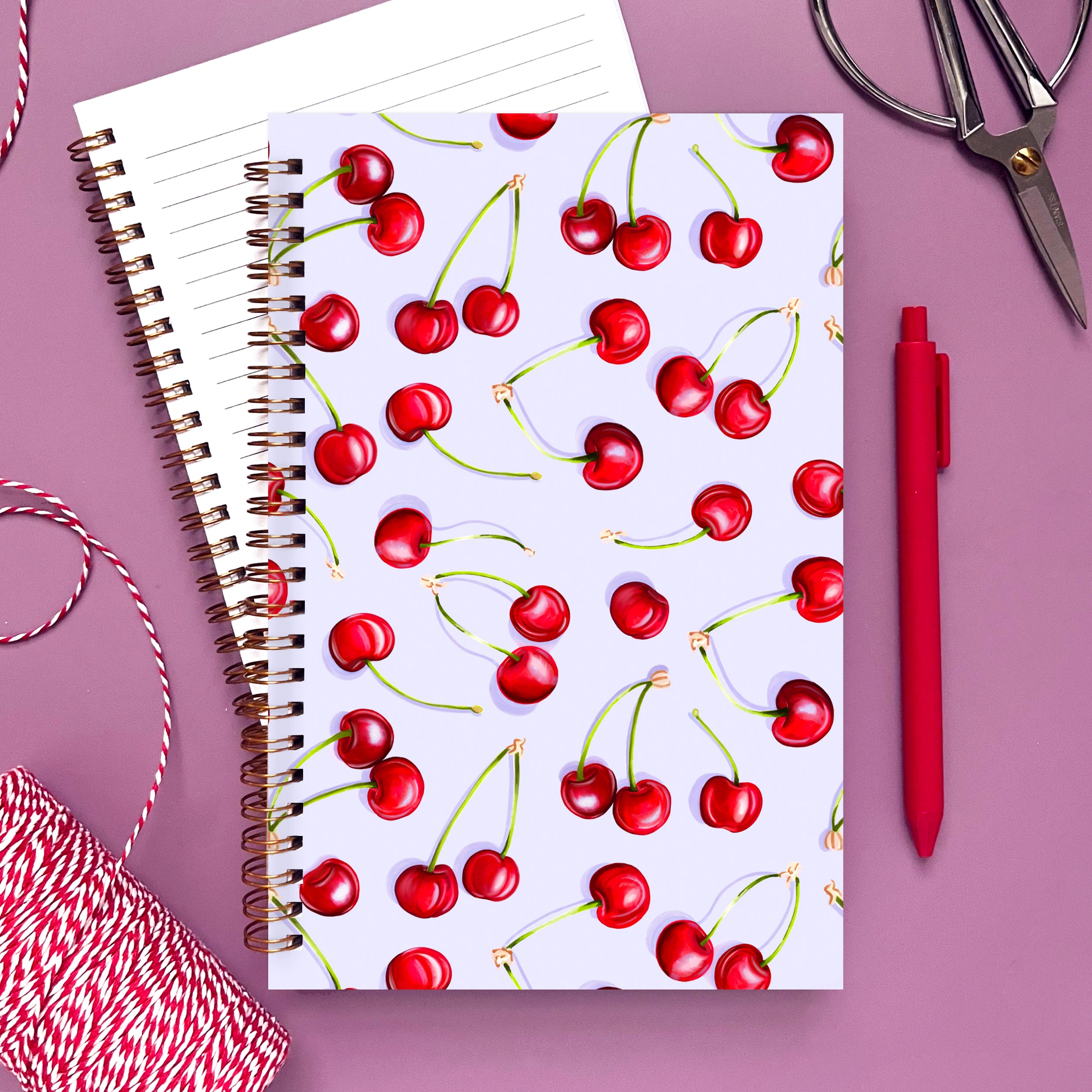 Notebook with bright red cherry illustrations on a light purple background.