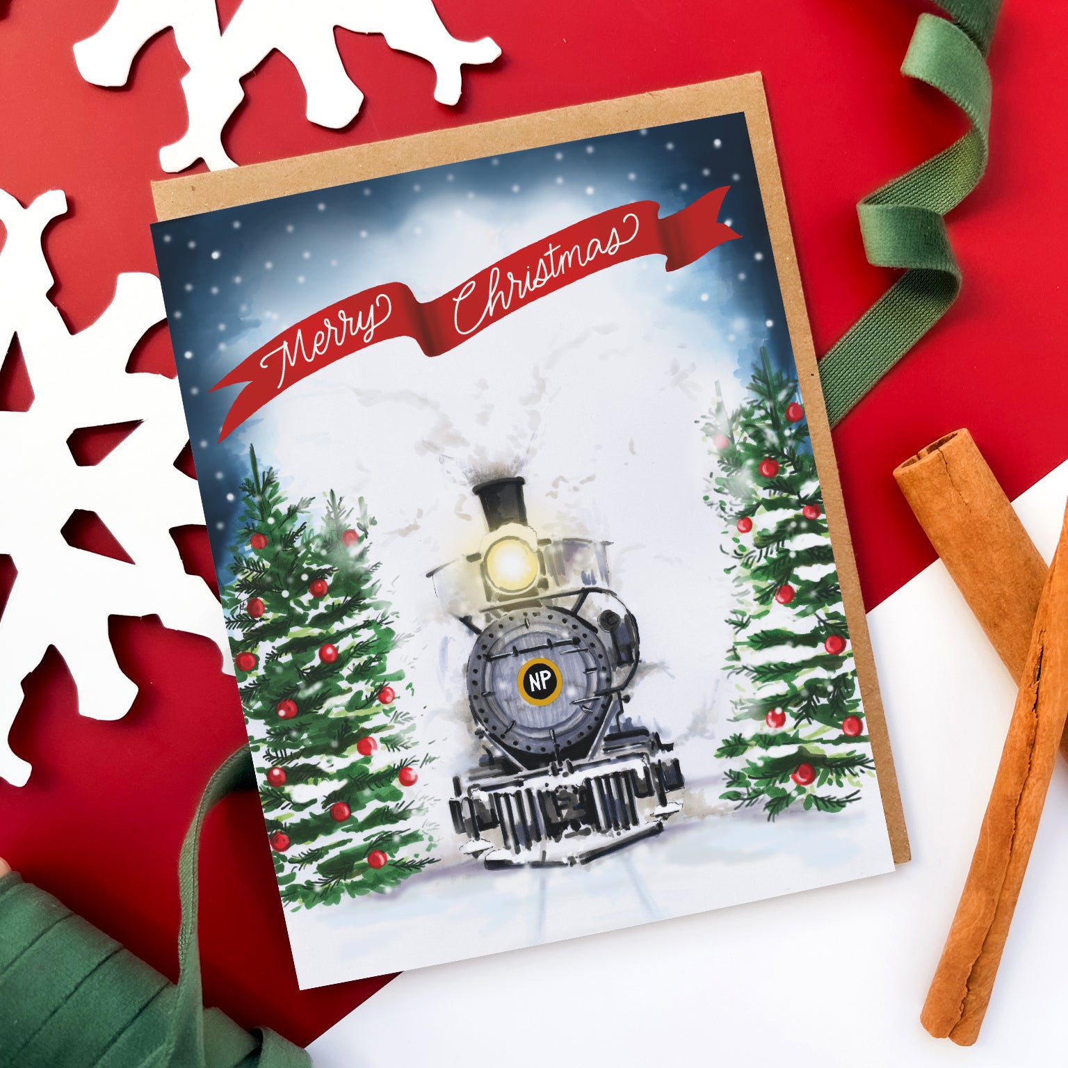 Greeting card with a vintage steam train driving through snowy pine trees, a red ribbon banner above reads 'Merry Christmas.'