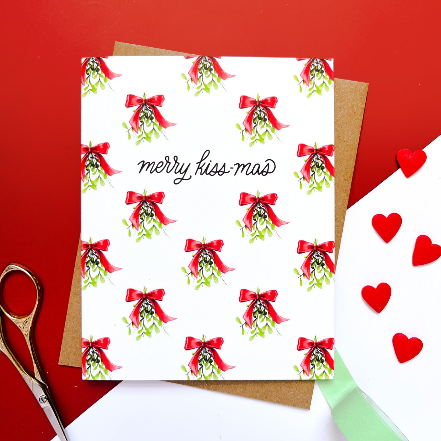 Holiday card with a repeating pattern of mistletoe tied with red bows and the text 'merry kiss-mas' in playful script in the center.