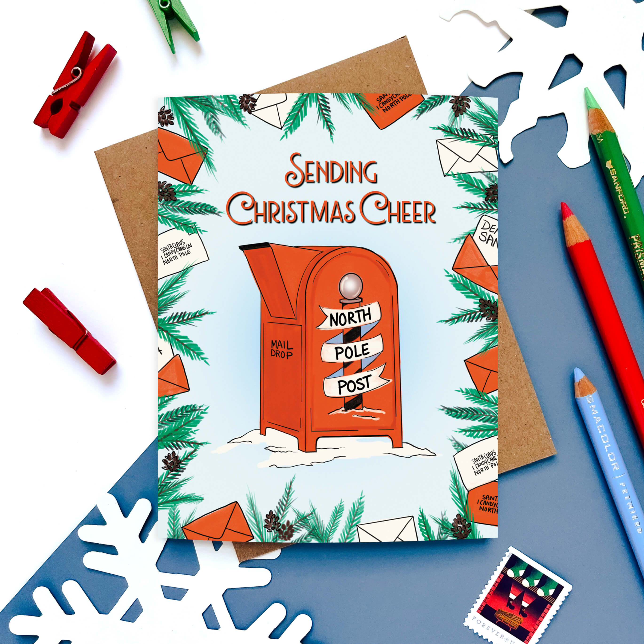 Christmas card with a red North Pole mailbox surrounded by letters and pine branches.