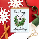 Christmas card with illustrated polar bear in a holiday wreath and the text 'have a beary merry Christmas' on a light blue background.