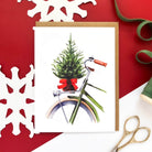 Christmas card with a green bicycle carrying a small decorated tree tied with a red bow on the back.