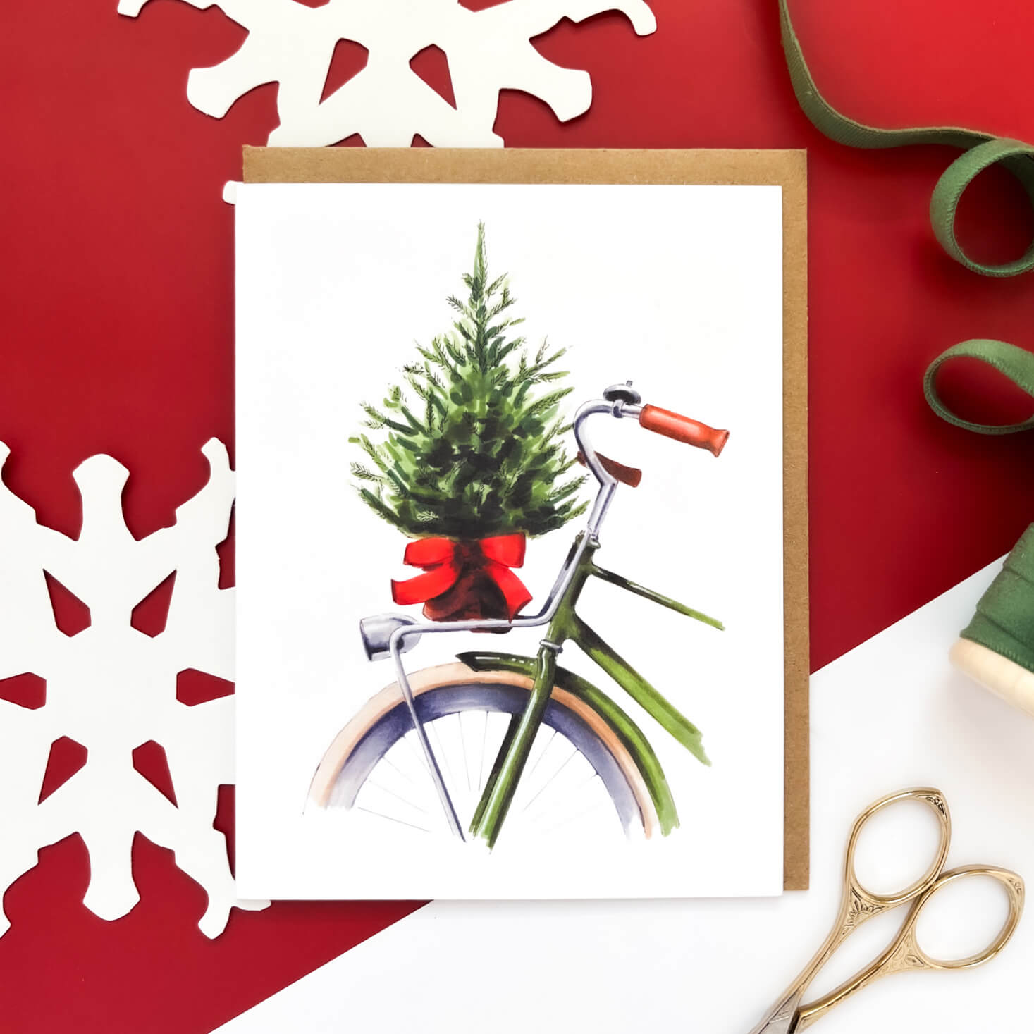 Christmas card with a green bicycle carrying a small decorated tree tied with a red bow on the back.