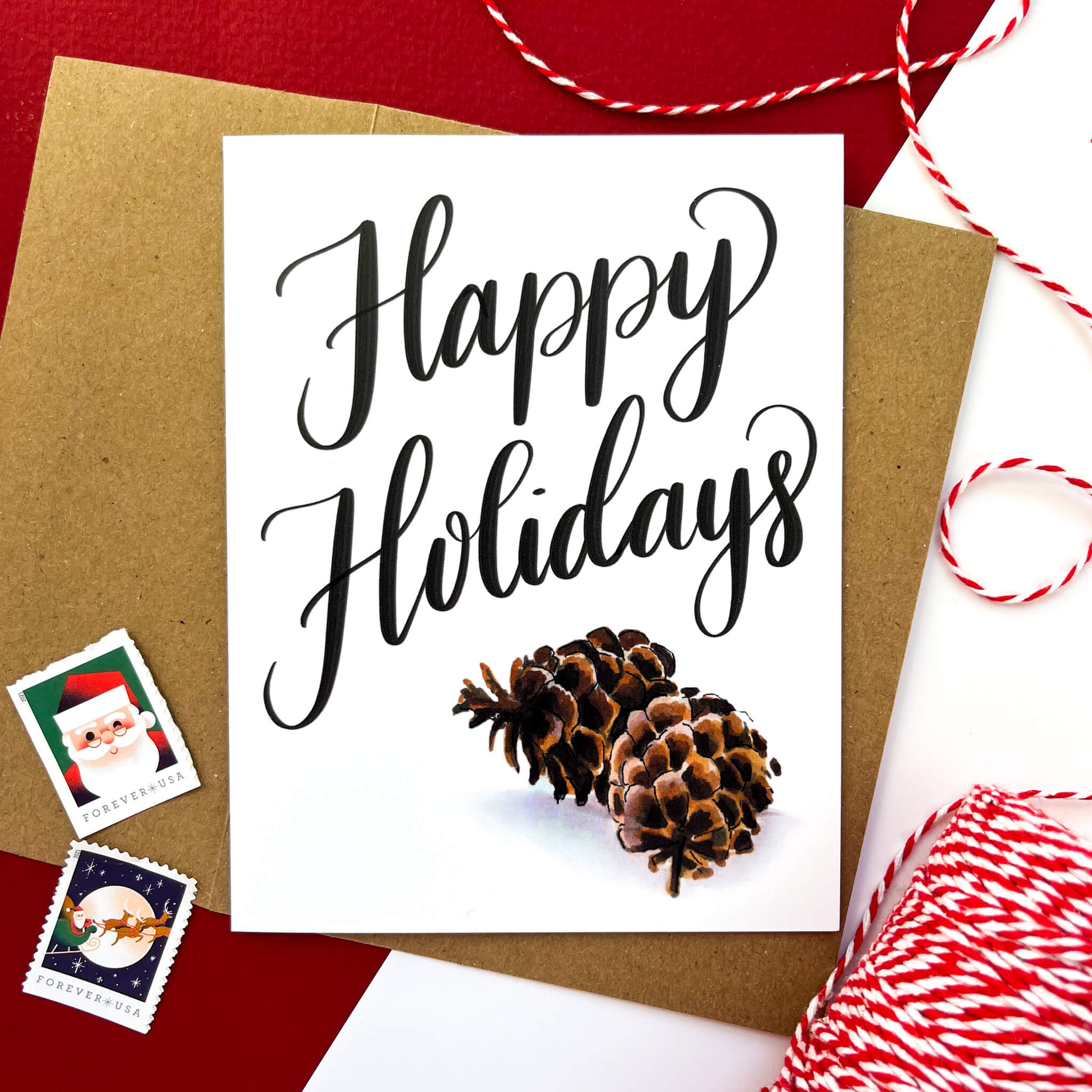 Greeting card with two realistic pinecones and the words 'Happy Holidays' in bold black script.