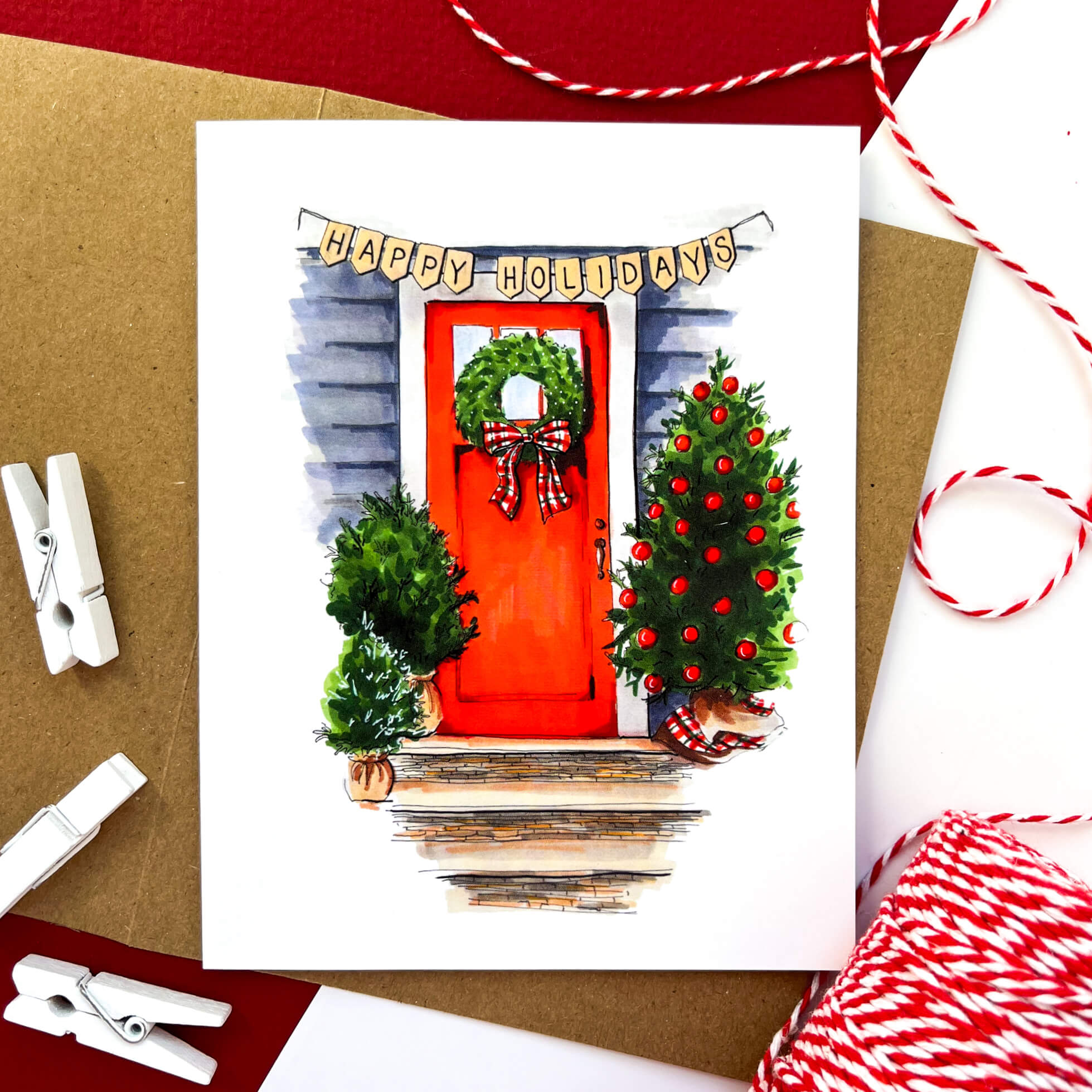 Greeting card showing a red front door decorated with a holiday wreath and trees, with a 'Happy Holidays' banner overhead.