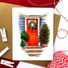 Greeting card showing a red front door decorated with a holiday wreath and trees, with a 'Happy Holidays' banner overhead.