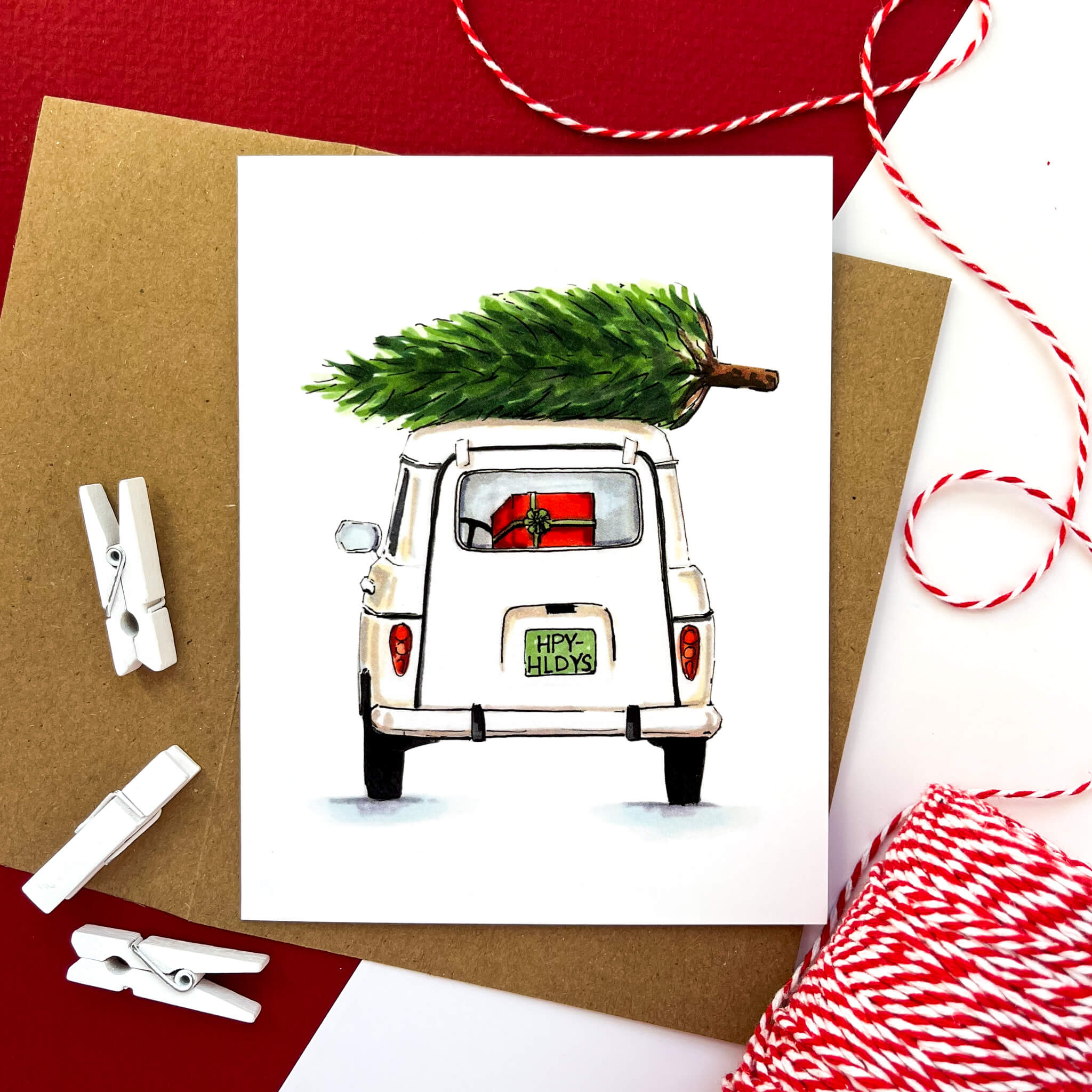 Holiday card showing a white retro car from the back, with a Christmas tree on the roof and gifts in the trunk.