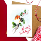 Greeting card with a watercolor-style robin sitting on a holly branch, red berries, and the text 'Happy Holidays' in red script.