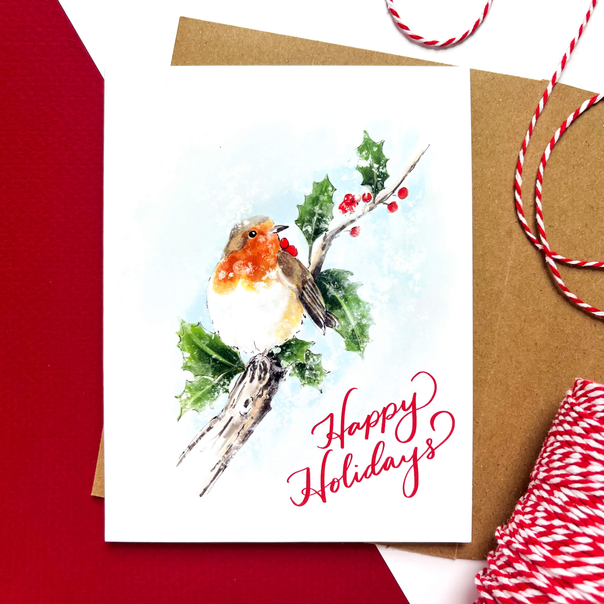 Greeting card with a watercolor-style robin sitting on a holly branch, red berries, and the text 'Happy Holidays' in red script.